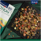 Bunte Haustierfutterkibble in Form von Tieren und Blumen, verstreut auf schwarzem Schiefer neben einer "Vitakraft Emotion"-Tüte.