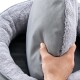 Eine Person hält ein weiches, graues Haustierbett mit einem plüschigen, hellgrauen Rand, das seinen Komfort und sein Design zeigt.