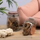 Zwei Glasbehälter gefüllt mit Hundeleckerlis, einer umgekippt, neben einem weichen rosa Haustiersofa und zwei weißen Seilspielzeugen auf einer Holzoberfläche.