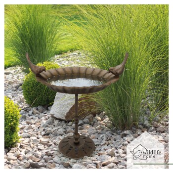 Ein dekorativer Vogelbad mit gewelltem Rand, mit zwei Vogelskulpturen am Rand, umgeben von Grün und Steinen.