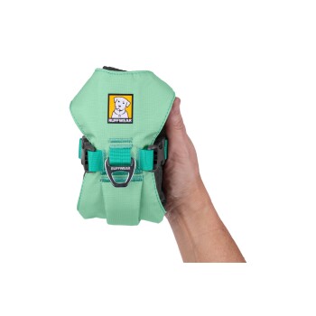 Eine Person hält ein mintgrünes Hundegeschirr mit einem Ruffwear-Logo, das verstellbare Riemen und einen Metallbefestigungspunkt hat.