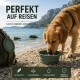 Brauner Hund mit schwarzem Geschirr trinkt Wasser aus einer zusammenklappbaren grünen Schale auf einem Bergpfad.