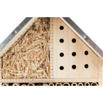 Holzinsektenhotel mit verschiedenen Fächern, einschließlich hohler Röhren und einem mit Netz abgedeckten Abschnitt, der mit Stroh gefüllt ist.