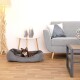 Ein kleiner braun-weißer Hund entspannt sich in einem gemütlichen grauen Haustierbett auf einem Holzboden, mit einem modernen grauen Sofa und dekorativen Gegenständen im Hintergrund.