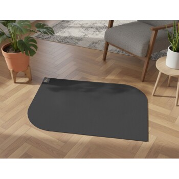 Schwarze Haustier-Futtermatte mit abgerundeten Ecken auf Holzboden neben Stuhl und Pflanzen, mit kleinem Logotag.