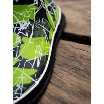 Nahaufnahme eines lebhaft grünen und schwarzen Haustierstiefels mit abstrakten weißen Designs, der auf einer Holzoberfläche ruht.