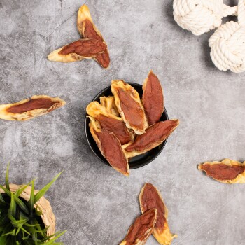 Eine schwarze Schüssel gefüllt mit Hundeleckerlis in Form von länglichen Blättern, mit einigen, die auf einer grauen Oberfläche verstreut sind.