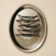 Cinq sardines entières alignées sur un plateau ovale en acier inoxydable sur un fond beige.