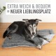Ein schwarzer und grauer Hund liegt bequem auf einem plüschigen, grauen Hundebett. Der Text oben lautet "EXTRA WEICH & BEQUEM = NEUER LIEBLINGSPLATZ."