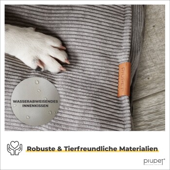 Nahaufnahme eines Hundebetts mit einer Hundepfote auf grauem Stoff, mit einem Lederetikett und Highlights für wasserabweisendes Kissen und haustierfreundliche Materialien.