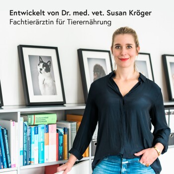 Frau in einem schwarzen Shirt steht vor einem Bücherregal mit Büchern über Haustierernährung, mit gerahmten Haustierfotos und Text darüber, Dr. Susan Kröger.