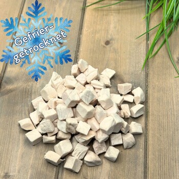 Haufen hellbeiger gefriergetrockneter Tierfutterwürfel auf Holzbrett, blaues Schneeflocken-Symbol mit der Aufschrift 'Gefrier-getrocknet'.