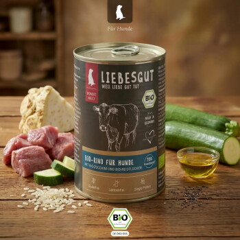 Dose Hundefutter von LIEBESGUT mit der Aufschrift 'Bio-Rind für Hunde' und Kuh-Illustration, umgeben von rohem Rindfleisch, Zucchini, Reis und einer kleinen Schale Öl.