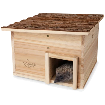 Ein Holz-Igelhaus mit einem mit Rinde bedeckten Dach, das einen kleinen Eingang und einen Igel, der herausblickt, zeigt. Das Haus ist mit "wildlife home" gebrandet.