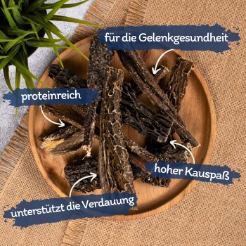 Ein Holzbrett zeigt Hundekauartikel, die auf Deutsch beschriftet sind: "für die Gelenkgesundheit," "proteinreich," "unterstützt die Verdauung," und "hoher Kauspaß."