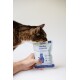Getigerte Katze schnüffelt an einer handlichen Tüte mit der Aufschrift 'Sardine Essential' und dem Text 'Snack gut. Tu Gutes. Fühl dich gut.'