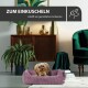 Ein gemütliches Hundebett in einem stilvollen Wohnzimmer mit einem kleinen Hund, der darin ruht. Text: "ZUM EINKUSCHELN" und "schafft ein gemütliches Ambiente."