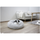 Ein kleiner schwarz-weißer Hund ruht sich in einem flauschigen grauen Haustierbett aus, mit einem hellgrauen Sofa und einem Holztisch in einem modernen Wohnzimmer.