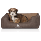 Ein kleiner, flauschiger Hund sitzt bequem in einem stilvollen braunen Haustierbett mit geripptem Design, das das Logo "KNUFFELWUFF" trägt.