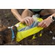 Eine Person, die eine Wasserflasche in einen leuchtend gelben Hunderrucksack steckt, während ein braun-weißer Hund in der Nähe steht.