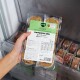 Hand hält eine Packung gefrorenes Hundefutter BARFER'S Komplett‑Mix Huhn & Lachs (400 g) in einem Gefrierschrank.