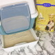 Eine Katzentoilette mit einer transparenten Klappe wird gezeigt, gefüllt mit hellfarbigem Katzenstreu. Daneben steht eine Tüte Lyra Power Tofu-Klumpenstreu.