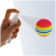 Eine Hand hält eine Sprühflasche, die einen bunten, gestreiften Haustier-Spielzeugball besprüht, der lebendige pinke, gelbe, grüne und blaue Farben zeigt.