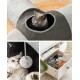 Eine graue Katze schaut aus einem grauen und schwarzen Tunnel, während eine andere Katze mit einem Pom-Pom-Spielzeug spielt und eine Hand nach einer Decke greift.