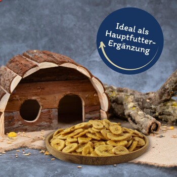 Holz-Haustierhaus mit einem Teller Bananenchips und dem Text „Ideal als Hauptfutter-Ergänzung“ in einem blauen Kreis.