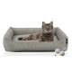 Eine entspannte getigerte Katze, die auf einem weichen, grauen Haustierbett liegt, begleitet von zwei verspielten Wollknäueln.
