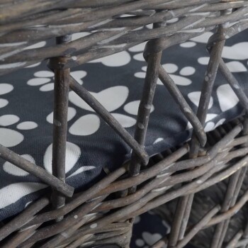 Nahaufnahme eines Haustierbettes aus geflochtenem Korb mit einem dunklen Stoffkissen, das weiße Pfotenabdruckmuster aufweist.