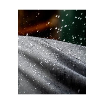 Nahaufnahme einer grauen Stoffoberfläche mit Wassertropfen, die ein strukturiertes Muster und einen verschwommenen Hintergrund zeigt.