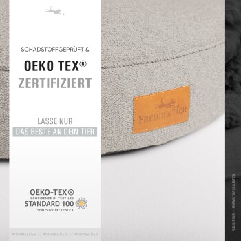 Ein graues Haustierbett mit einem Lederetikett mit der Aufschrift "Freudentier", mit Informationen über Oeko-Tex-Zertifizierung und Sicherheitsstandards.