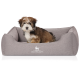 Ein kleiner, flauschiger Hund sitzt bequem in einem grauen Haustierbett mit dem Logo "KNUFFELWUFF", das prominent auf der Vorderseite angezeigt wird.