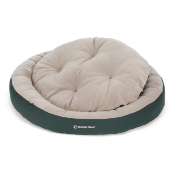 Ein plüschiges, rundes Haustierbett mit einem weichen beigen Kissen und einem dunkelgrünen äußeren Rand, mit dem Logo 'Doctor Bark'.