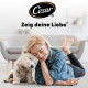 Cesar-Logo und Text 'Zeig deine Liebe' über einer lächelnden Frau, die auf dem Boden liegt und einen kleinen weißen Hund im Wohnzimmer kuschelt.
