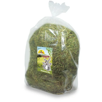 Eine durchsichtige Plastiktüte gefüllt mit grünem Heu, beschriftet mit "JR FARM Bergwiesen-Heu", mit einer Cartoonkaninchenillustration und einer malerischen Kulisse.