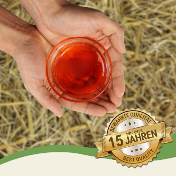 Hände, die eine kleine rote Schale mit Flüssigkeit halten, Heuhintergrund und ein goldener Abzeichen mit der Aufschrift „15 Jahren Best Quality“.