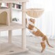 Eine verspielte orange-weiße Katze streckt sich zu einem beigen Katzenbaum mit einer hängenden Hängematte, in einem hellen, luftigen Raum.