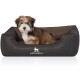 Ein kleiner, flauschiger Hund sitzt bequem in einem stilvollen schwarzen Hundebett mit braunem Innenraum, mit dem Logo 'KNUFFELWUFF.'