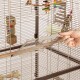 Eine Hand öffnet eine Schiebetür an einem Vogelkäfig und zeigt bunte Spielzeuge und eine Sitzstange im Inneren des Käfigs.