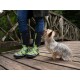 Eine Person in bunten, grün und schwarz gemusterten Gummistiefeln steht auf einer Holzbrücke, während ein kleiner, flauschiger Hund zu ihnen aufblickt.