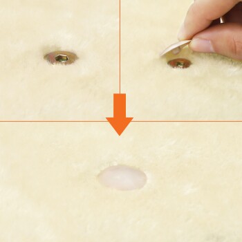 Eine Hand entfernt ein rundes Klebe-Patch von einer weichen, flauschigen Oberfläche mit einem sichtbaren Loch, was eine Funktion eines Haustierprodukts demonstriert.