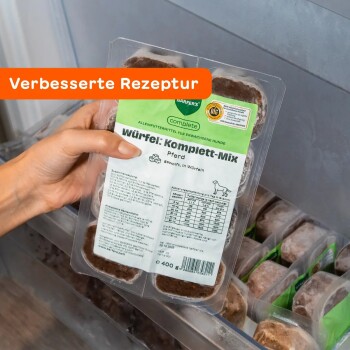 Hand hält Packung gefrorener Hundefutterwürfel mit der Aufschrift „Würfel: Komplett‑Mix Pferd“ und orangefarbenem Banner „Verbesserte Rezeptur“.