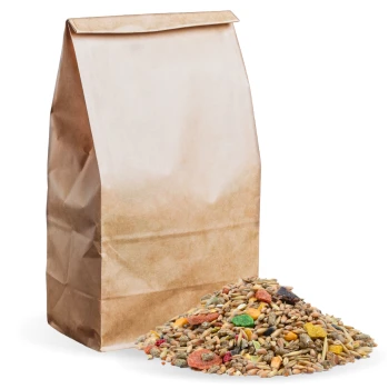 Eine braune Papiertüte mit Haustierfutter steht neben einem bunten Haufen gemischter Samen, Getreide und getrockneter Früchte auf einem weißen Hintergrund.