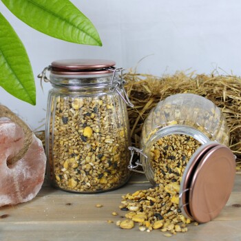 Zwei Glasbehälter mit Tierfutter, einer umgekippt, umgeben von Heu, einem rosa Salzblock und grünen Blättern.