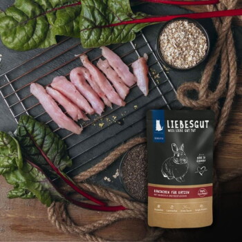 LIEBESGUT-Katzenfutterbeutel mit der Aufschrift "Kaninchen für Katzen" neben rohen Kaninchenstreifen, Mangoldblättern und Haferflocken.