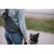 Eine Person in einer Jeansjacke steht mit dem Rücken zur Kamera und trägt eine schwarze PAIKKA-Haustieraccessoire-Tasche, während ein Hund zu ihnen aufblickt.