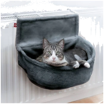 Eine graue Katze mit grünen Augen, die in einem gemütlichen, grauen Katzenbett liegt, das an einem Heizkörper befestigt ist.