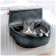 Eine graue Katze mit grünen Augen, die in einem gemütlichen, grauen Katzenbett liegt, das an einem Heizkörper befestigt ist.